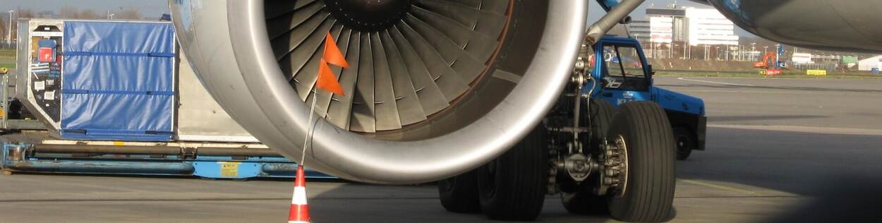 Two triangular orange safety flags and an orange safety cone in front of an aeroplane turbine engine.