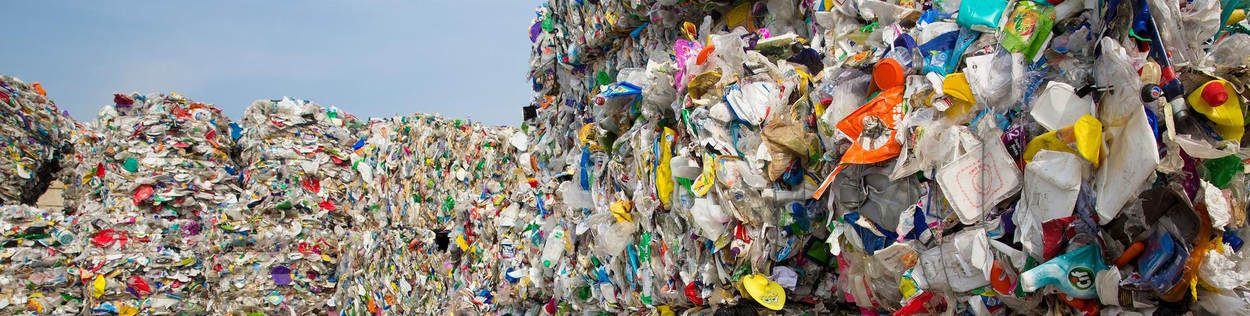 Stapels vierkante balen plastic staan bij elkaar. De balen bestaan uit afgedankt plastic zoals petflessen en snackbakjes.