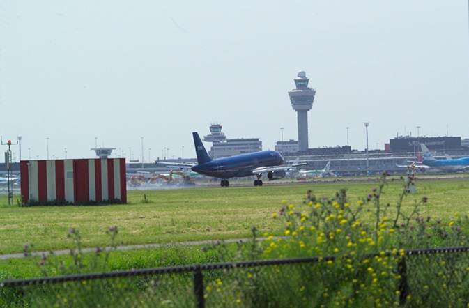 Een KLM-vliegtuig stijgt op van een van de landingsbanen bij Schiphol. Op de achtergrond is de Schipholtoren zichtbaar.